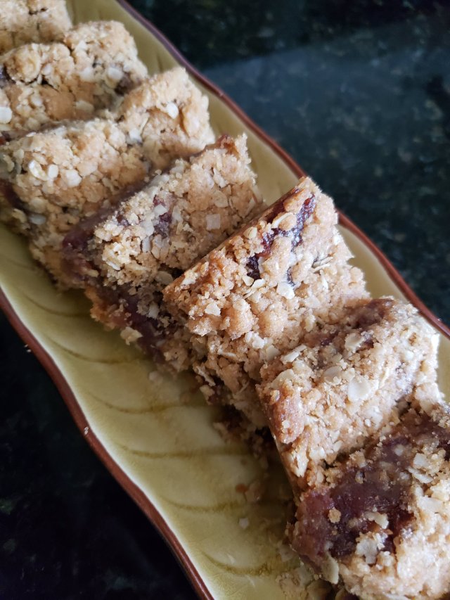 a layer of date filling sandwiches between 2 layers of oats and nuts on a long golden ceramic tray