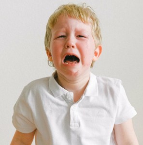 blond haired boy in a white polo shirt sobbing, tears from his eyes run down his cheeks